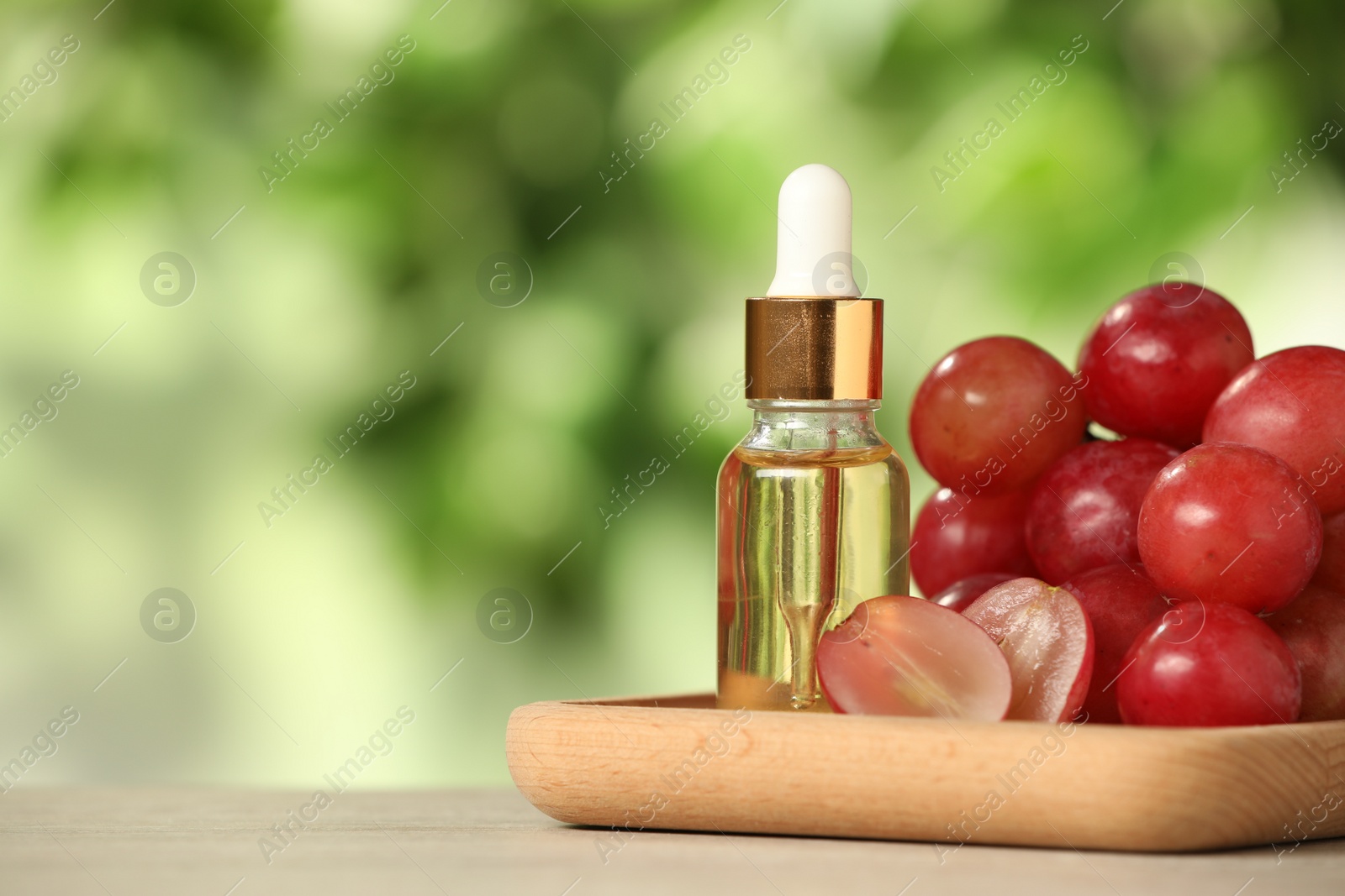 Photo of Fresh grapes and bottle of essential oil on wooden table. Space for text