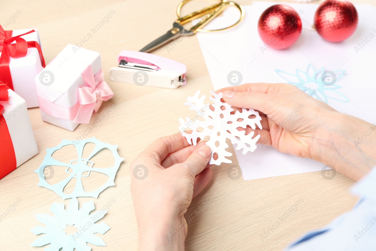 Photo of Woman making paper snowflake at wooden table, closeup