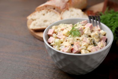 Photo of Tasty Olivier salad with boiled sausage in bowl on wooden table, space for text