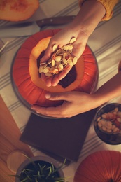 Woman making pumpkin jack o'lantern at table, top view. Halloween celebration