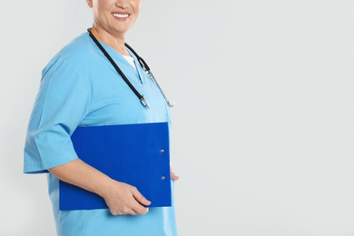 Photo of Mature doctor with clipboard on light grey background, closeup. Space for text