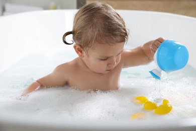 Cute little girl playing in foamy bath at home