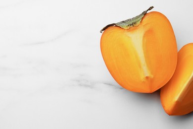 Photo of Pieces of delicious ripe persimmons on white marble table, space for text