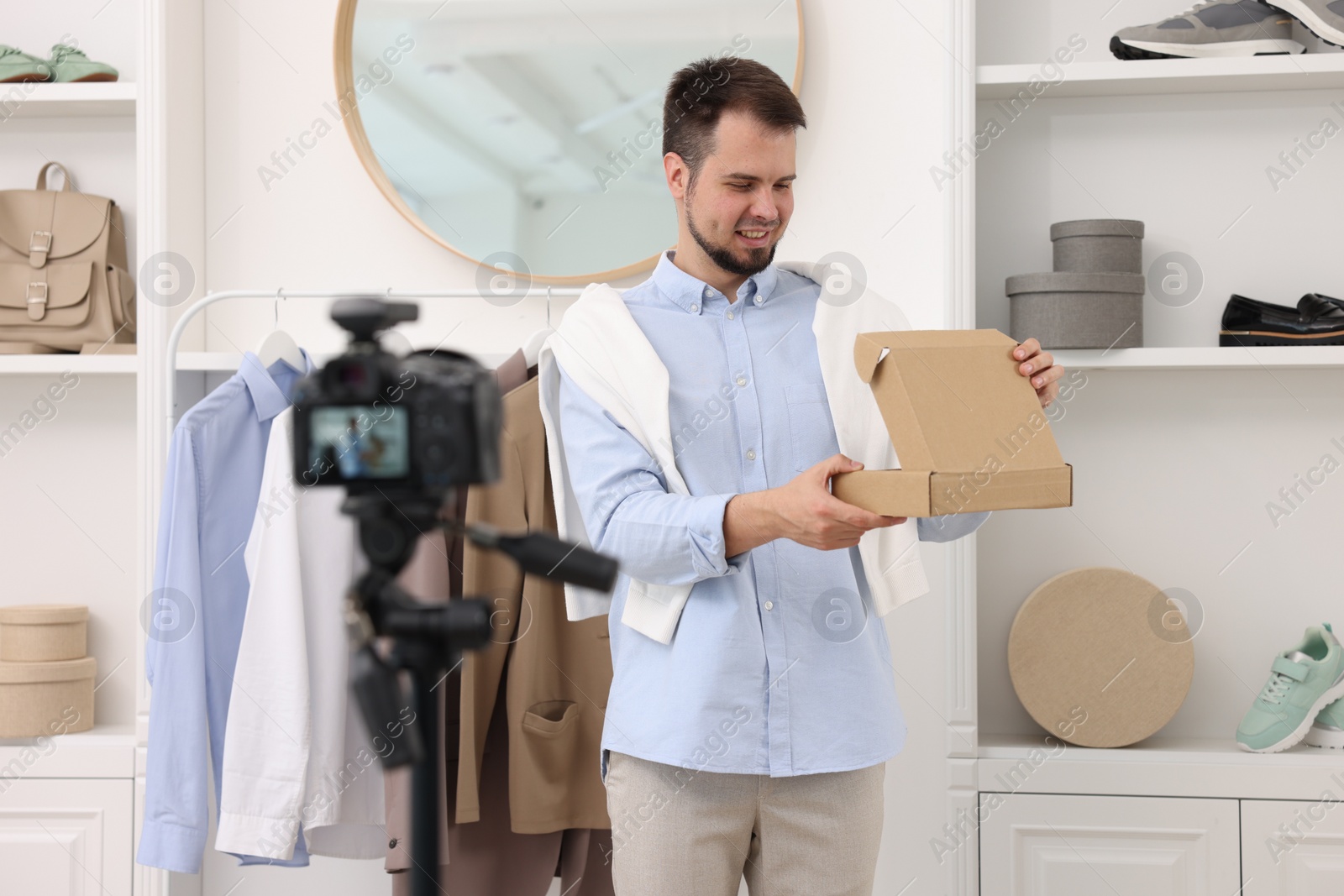 Photo of Smiling fashion blogger opening cardboard box while recording video at home