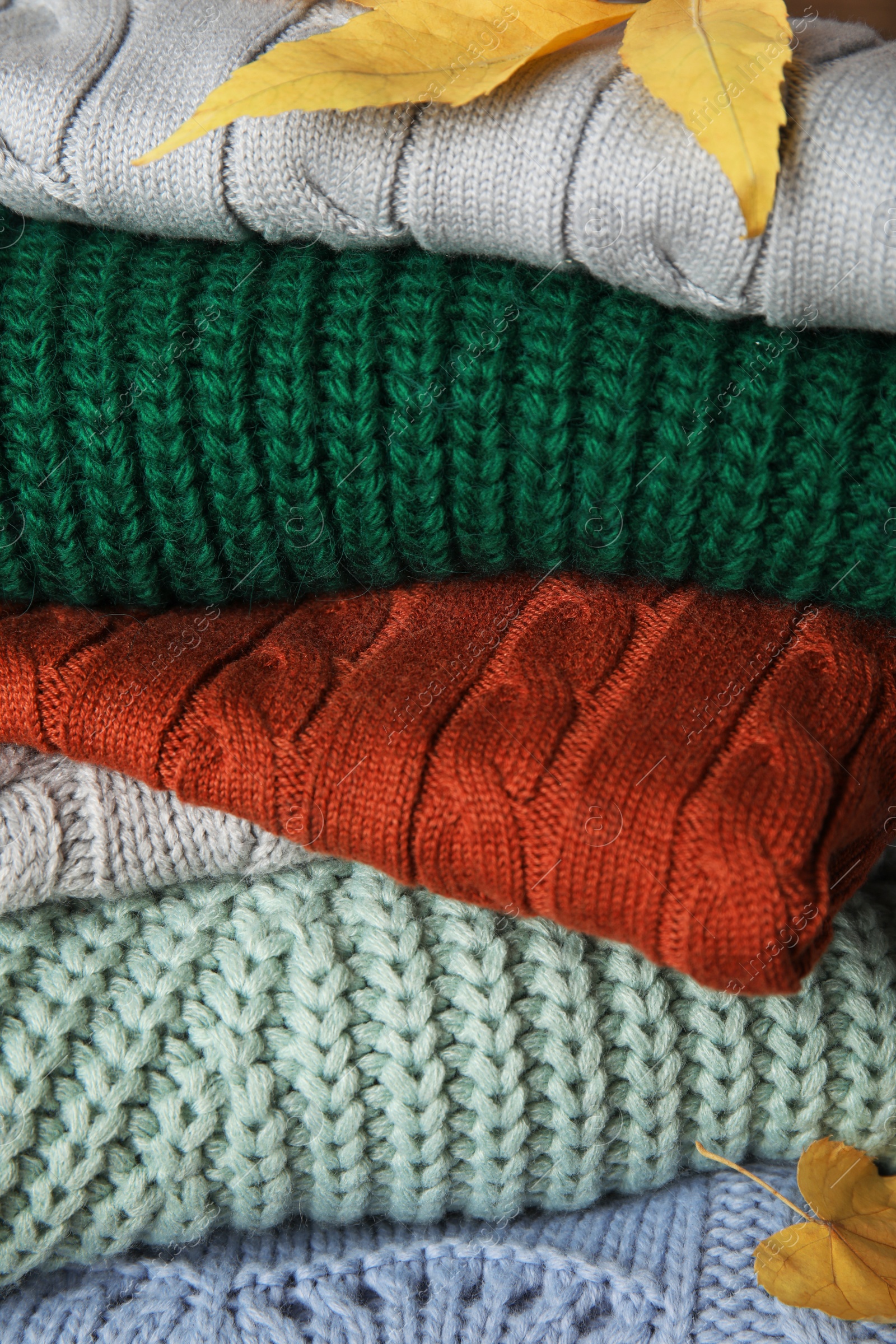 Photo of Heap of warm clothes with autumn leaves, closeup