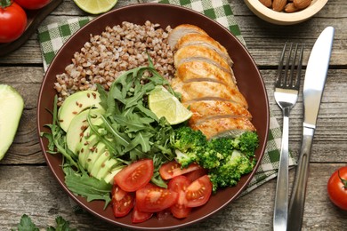 Healthy meal. Tasty products in bowl, ingredients and cutlery on wooden table, flat lay