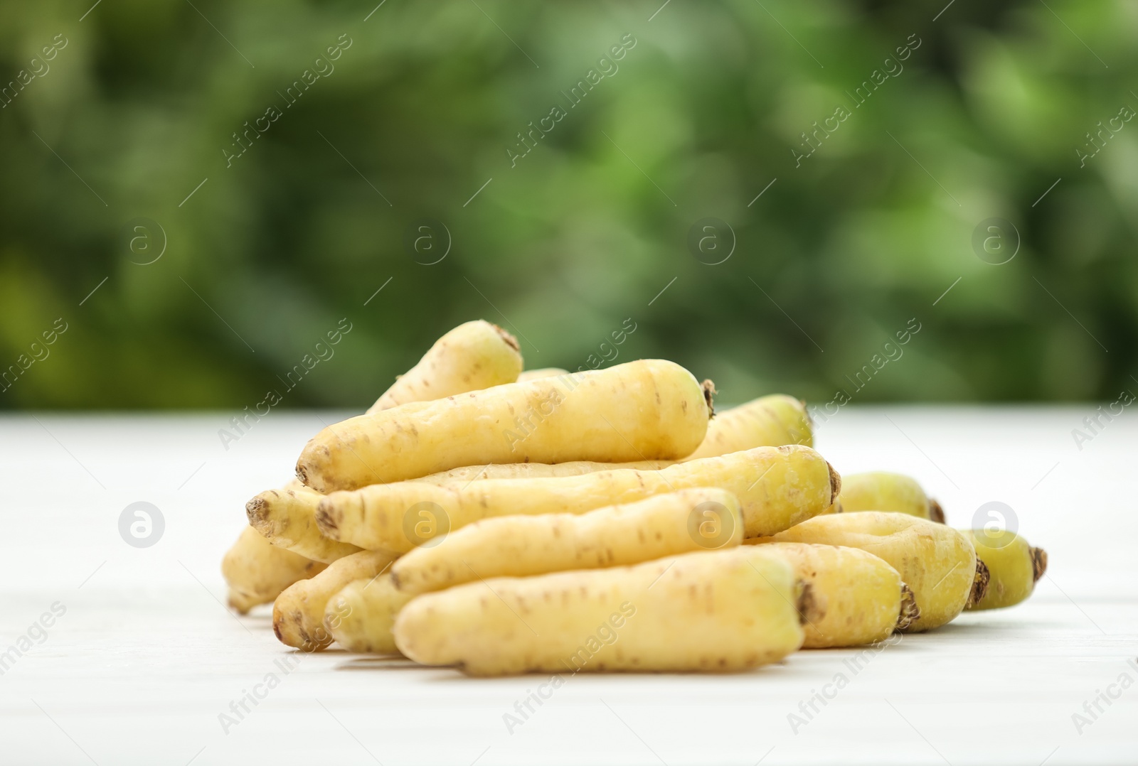 Photo of Raw white carrots on wooden table against blurred background