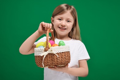 Photo of Easter celebration. Cute girl with basket of painted eggs on green background