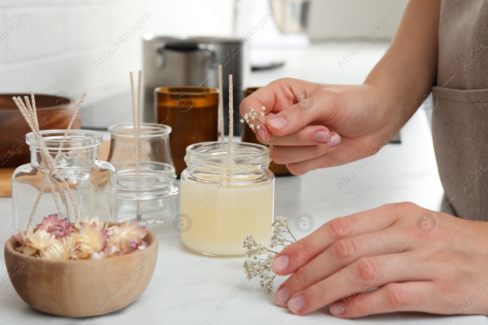 Photo of Woman decorating homemade candle with gypsophila flowers at table indoors, closeup