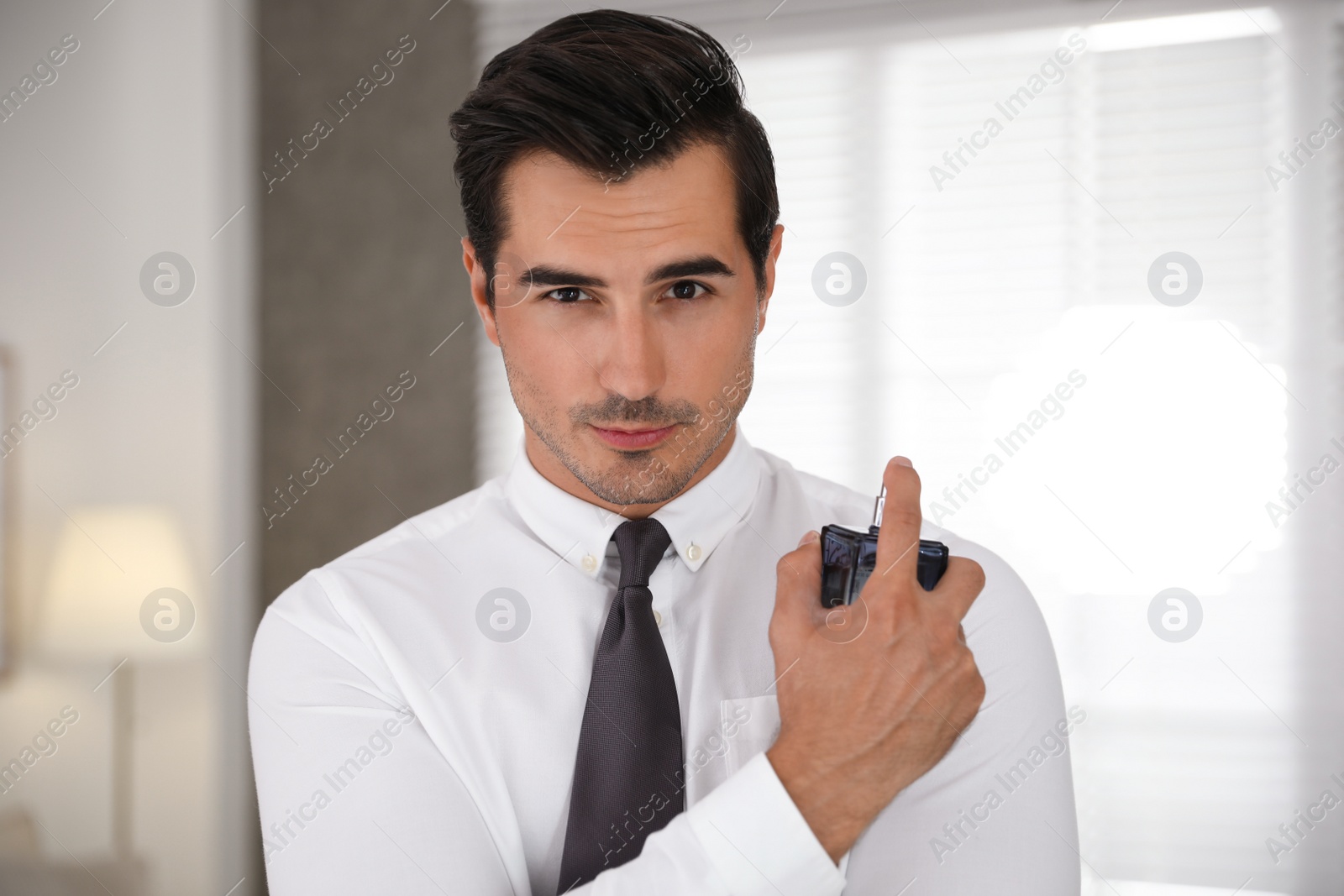 Photo of Handsome young man using luxury perfume indoors