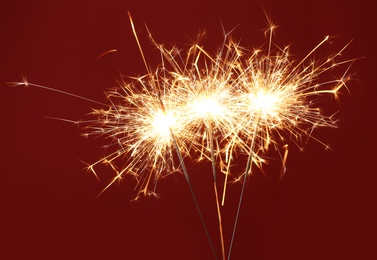 Photo of Bright burning sparklers on red background, closeup
