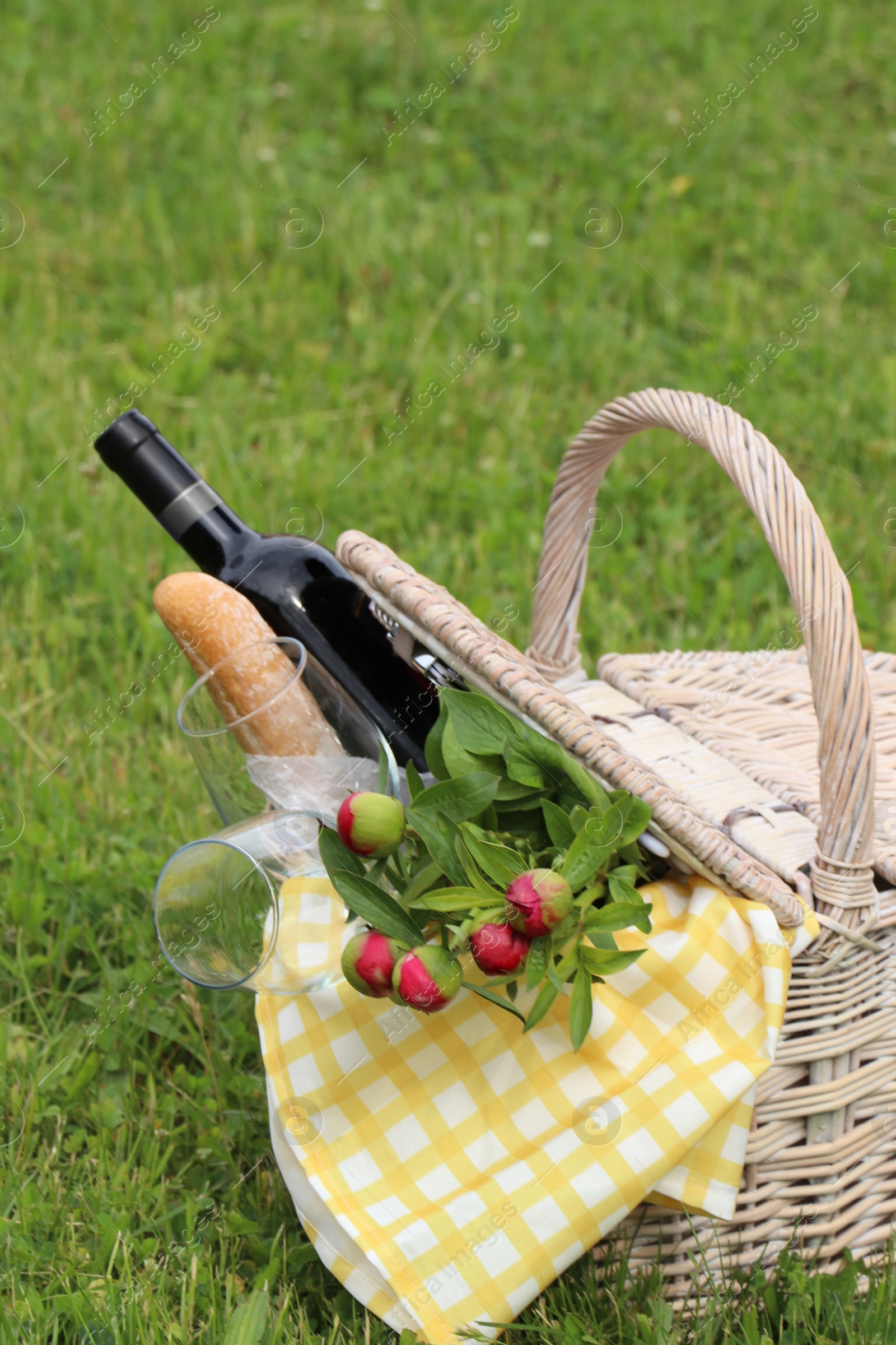 Photo of Picnic basket with wine, bread and flowers on green grass outdoors