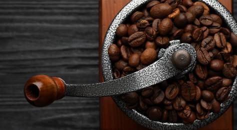 Photo of Vintage manual coffee grinder with beans on black wooden table, top view