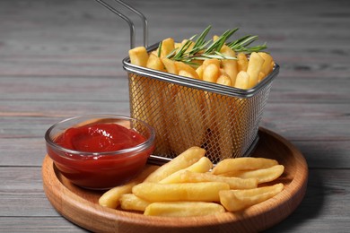 Photo of Tasty French fries, rosemary and ketchup on grey wooden table, closeup