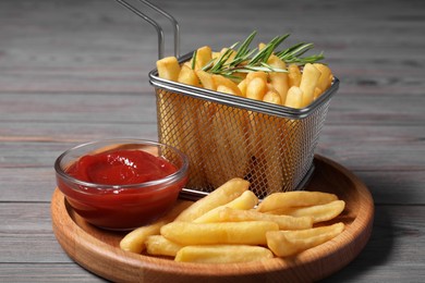 Tasty French fries, rosemary and ketchup on grey wooden table, closeup