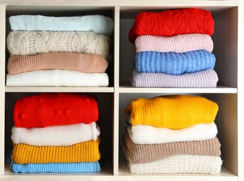 Folded colorful winter sweaters on shelves as background