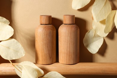 Photo of Wooden bottlescosmetic product and dried leaves on dark beige background