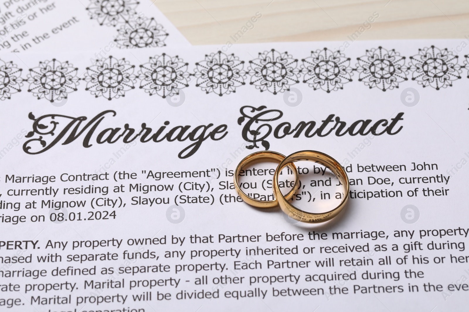 Photo of Marriage contracts and gold rings on light wooden table, above view