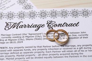 Marriage contracts and gold rings on light wooden table, above view