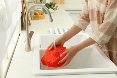 Photo of Woman washing beeswax food wrap under tap water in kitchen sink, closeup