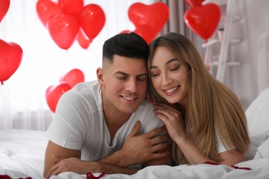 Lovely couple on bed in room decorated with heart shaped balloons. Valentine's day celebration