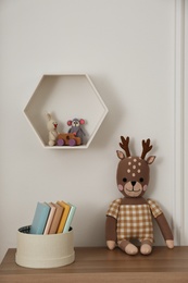Photo of Soft deer toy and books on wooden table in baby room. Interior design