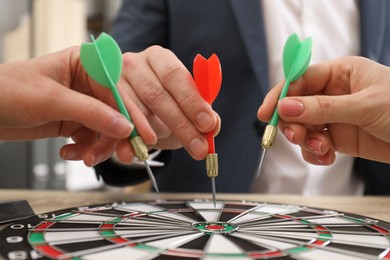 Business targeting concept. People with darts aiming at dartboard at table, closeup