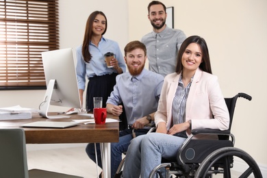 Photo of Young woman in wheelchair with colleagues at workplace