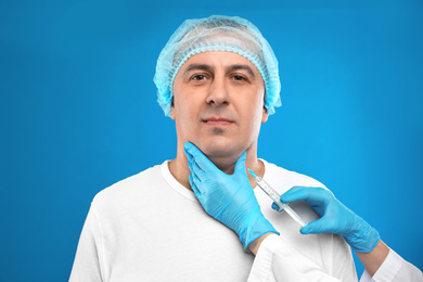 Mature man with double chin receiving injection on blue background