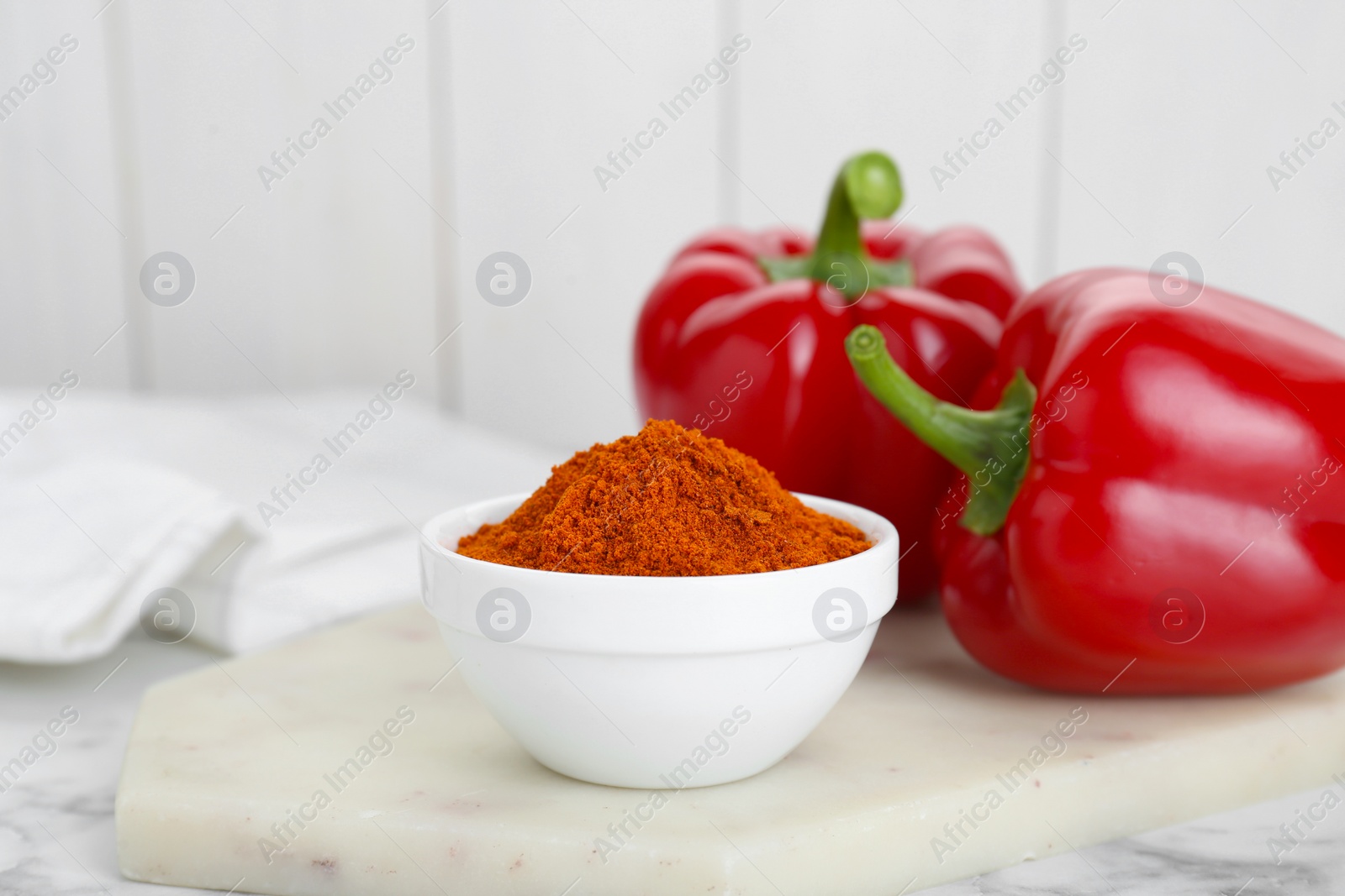 Photo of Bowl with aromatic paprika powder and fresh bell peppers on white marble table
