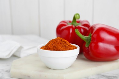 Bowl with aromatic paprika powder and fresh bell peppers on white marble table