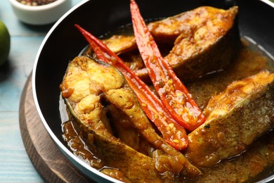 Photo of Tasty fish curry in frying pan on light blue table, closeup. Indian cuisine