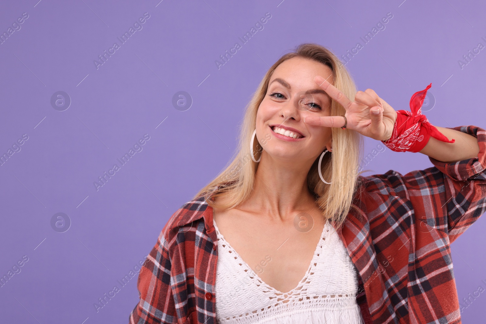 Photo of Portrait of happy hippie woman showing peace sign on purple background. Space for text