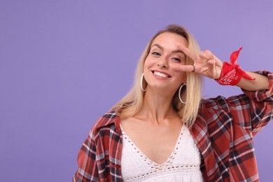 Photo of Portraithappy hippie woman showing peace sign on purple background. Space for text