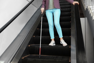 Photo of Blind person with long cane on escalator indoors
