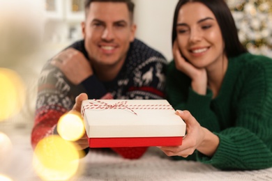 Happy couple with Christmas gift box at home, focus on hands