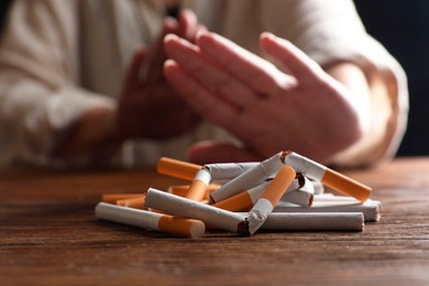 Photo of Stop smoking. Woman making stop gesture at wooden table, focus on whole and broken cigarettes