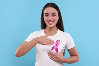 Photo of Beautiful happy woman with pink ribbon on light blue background. Breast cancer awareness