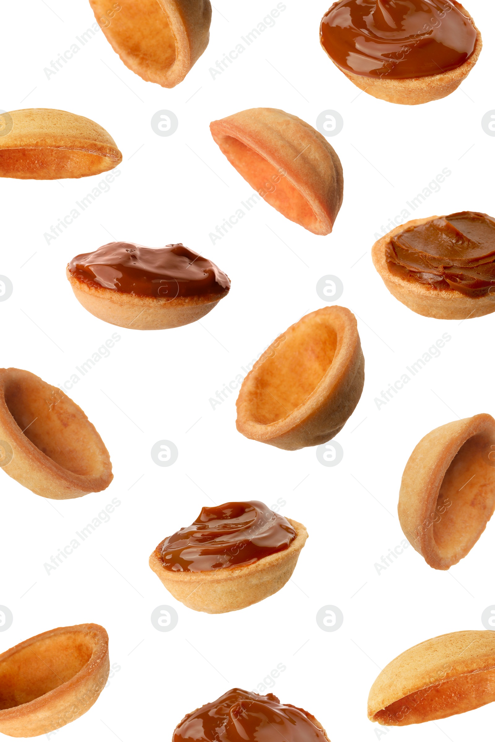 Image of Many empty and filled with caramelized condensed milk nut shell shaped cookie parts falling on white background