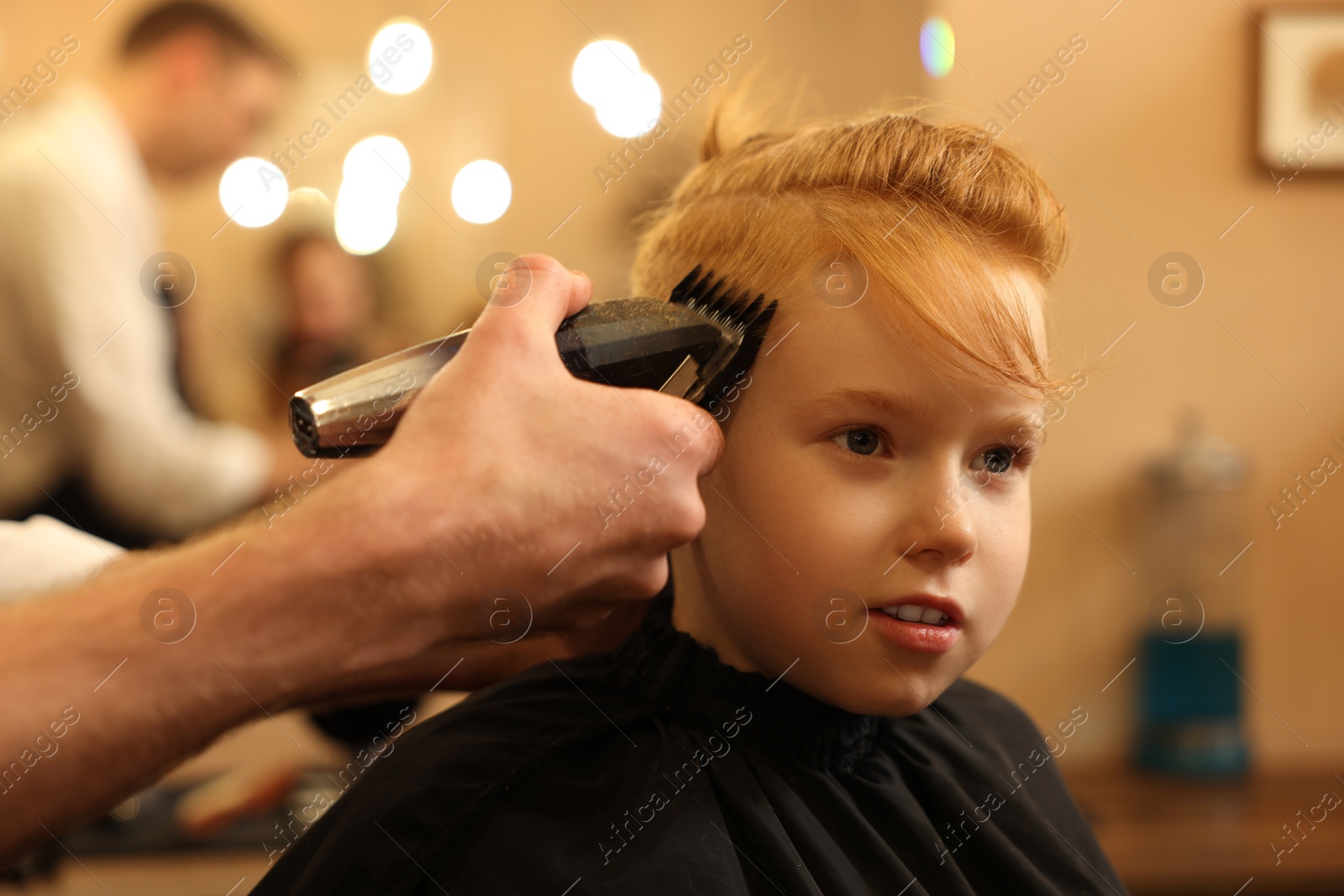 Photo of Professional hairdresser cutting boy's hair in beauty salon, closeup