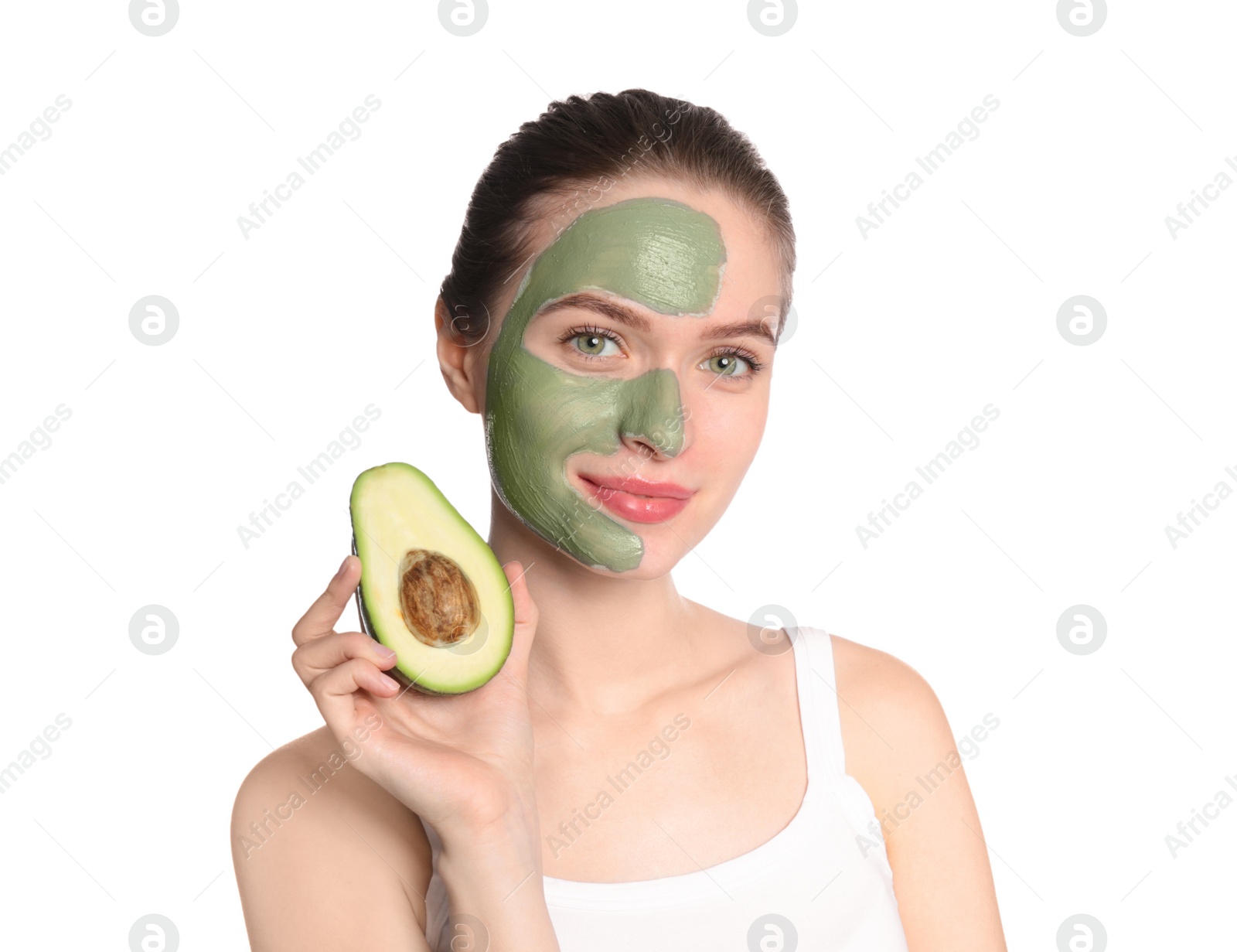 Photo of Young woman with clay mask on her face holding avocado against white background. Skin care