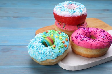 Photo of Sweet glazed donuts decorated with sprinkles on light blue wooden table, space for text. Tasty confectionery