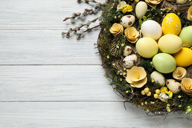 Photo of Decorative wreath with Easter eggs on white wooden background, top view. Space for text