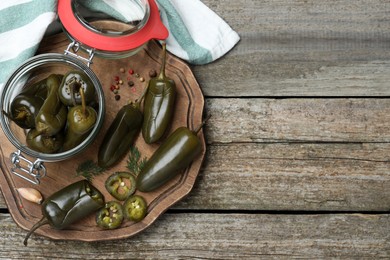 Pickled green jalapeno peppers and spices on wooden table, flat lay. Space for text