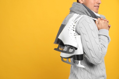 Happy man with ice skates on yellow background, closeup. Space for text