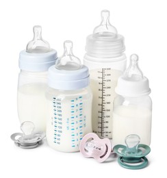 Many feeding bottles with infant formula and pacifiers on white background