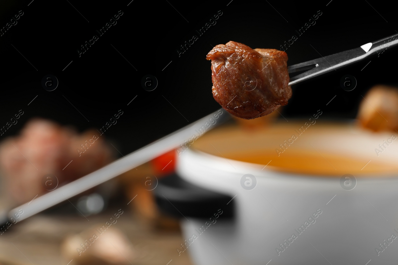 Photo of Fork with cooked meat and blurred fondue pot on background, closeup. Space for text