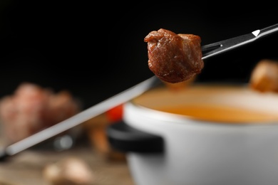 Photo of Fork with cooked meat and blurred fondue pot on background, closeup. Space for text