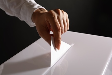 Woman putting her vote into ballot box on black background, closeup