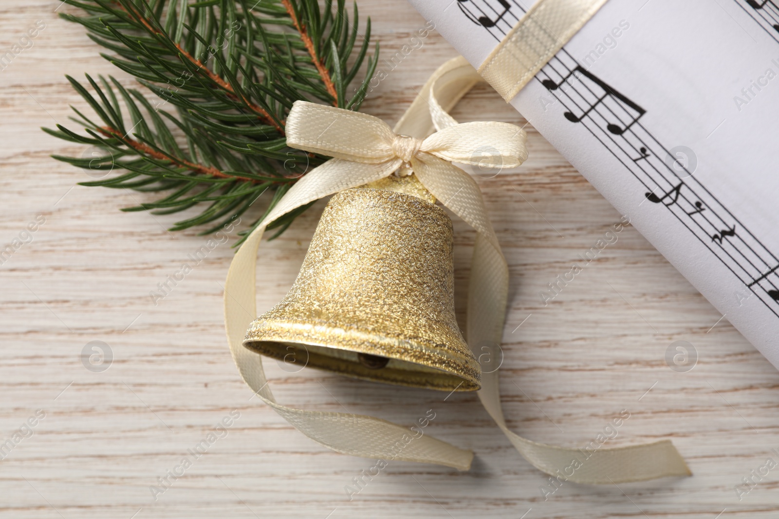 Photo of Golden shiny bell with bow, music sheet and fir twig on wooden table, flat lay. Christmas decoration